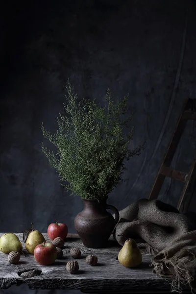 Güzel natürmort ceviz, armut, elma ve sürahi ile karanlık Studio ahşap masa üzerinde yeşil bitkiler