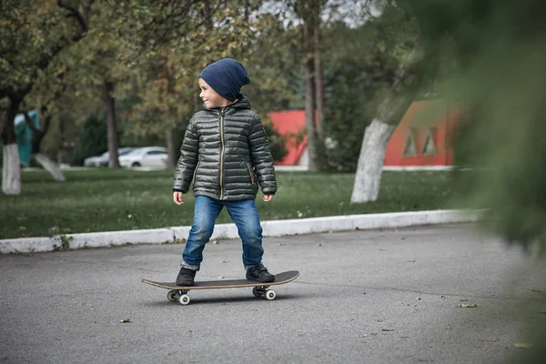 Açık havada gri skate board sürme koyu gri ceket, koyu mavi kap ve mavi jeans, şirin küçük çocuk  