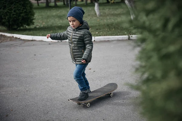 Açık havada gri skate board sürme koyu gri ceket, koyu mavi kap ve mavi jeans, şirin küçük çocuk  