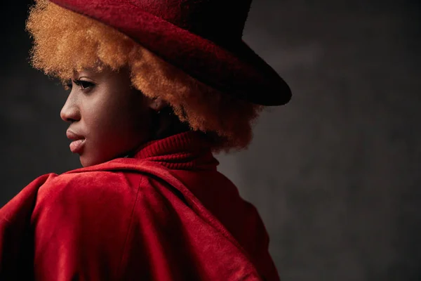 Portrait of beautiful black young smiling female model wearing red sweater and jacket, with red curly hair and red hat in studio with red background