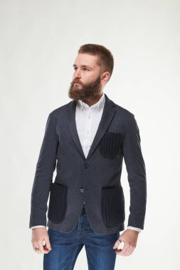 Çekici genç seksi ciddi adam modeli koyu gri ceket, beyaz gömlek ve koyu mavi pantolon Işık Studio poz sakallı 