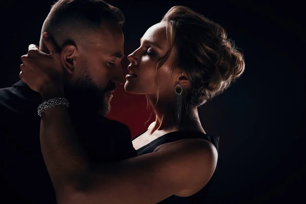 İpeksi siyah elbise ve şık takı ve yakışıklı sakallı adam ile harika bir smokin giyiyor tutkulu lüks kadın sarışın kabarık saçlı koyu Studio'da poz
