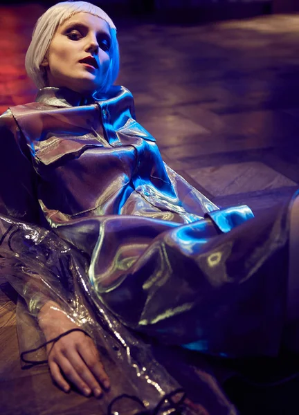 Futurystyczny neon oświetlone portret dziewczynki z białym bob fryzura sobie jedwabiście bluzka i Płaszcz przeciwdeszczowy przezroczysty, siedząc na podłodze — Zdjęcie stockowe