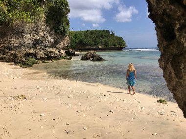 Bali vahşi bir kıyısında bir ipek elbise şaşırtıcı ve mutlu sarışın kadın yürüyor