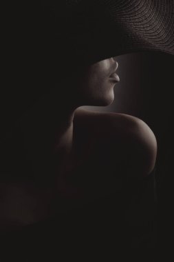Dramatik karanlık studio siyah geniş şapka ve siyah elbise seksi kadın portresi. Gizli yarım yüz.