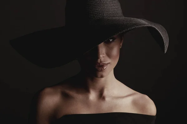 黒の広い帽子と黒のドレスでエレガントなセクシーな女性の暗いスタジオ ポートレート — ストック写真
