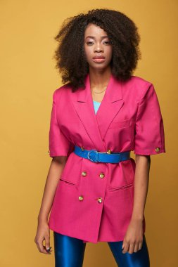 Afro saç modeli ile çekici genç Afrikalı kız Güzellik Portresi. Pembe ceket, mavi tozluk ve Sarı zemin üzerine poz kemer giyen kız. Stüdyo vurdu