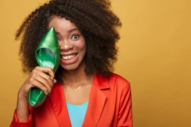 Afro saçlı Afrika kız portre renkli yakından. Turuncu ceket giyen gülümseyen kız yeşil ayakkabı göz tutar. Stüdyo vurdu