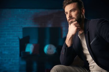 Stüdyo koyu saç, sakal ve bıyık üzerinde koyu mavi ceket, gri pantolon ile ciddi adam portresi. Saat ve varil ile Mavi ışıklı tuğla arka plan