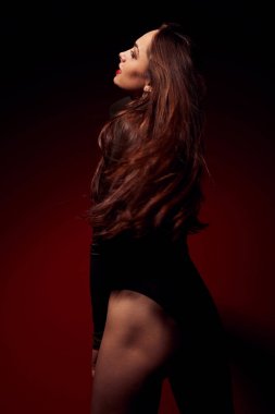 Güzel, harika, baştan çıkarıcı kadın uzun siyah saçlı ve koyu kırmızı arka plan üzerinde siyah elbise poz kırmızı dudaklar ile karanlık portresi. Moda, glamour, kavram. 
