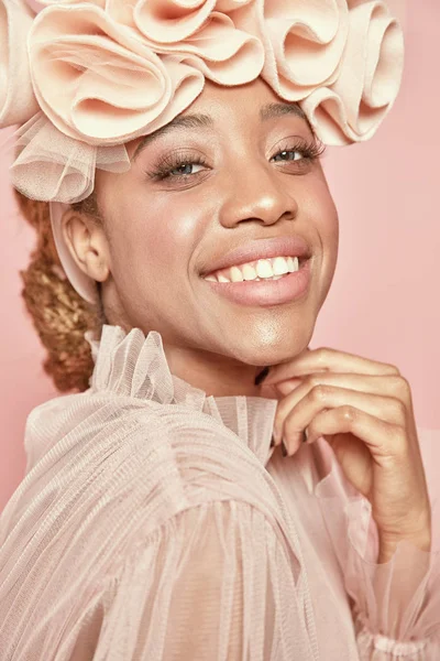 Close-up portrait of beautiful black smiling woman with light hair and green eyes wearing powder pink tulle dress and big frill hairband