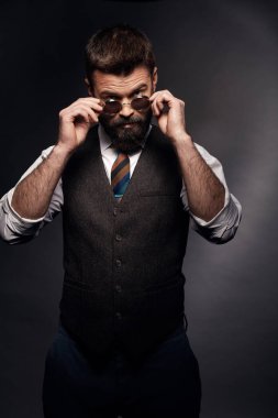 Koyu saç, bıyık ve sakal beyaz gömlek, kahverengi yelek ve renkli kravat üzerinde yuvarlak güneş gözlüğü alarak ciddi adam düşük anahtar portresi