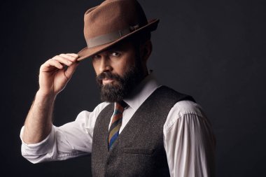 Stüdyo koyu saç, bıyık ve sakal Beyaz gömlekli olan yakışıklı adam portresi, kahverengi yelek, renkli kravat, kahverengi şapka kafasına tutarak. Eski moda stil.