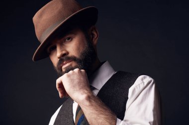 Stüdyo portre yakışıklı adamın giydiği beyaz gömlek, kahverengi yelek, renkli kravat, kahverengi şapka koyu saç ve sakal, elinde tutan bıyık. Eski moda stil, beyefendi.