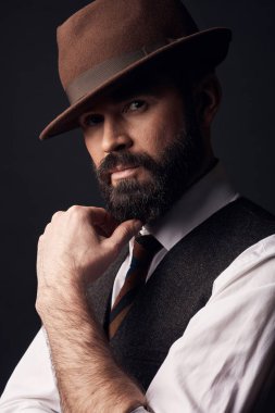 Stüdyo portre siyah saçları ve bıyığı beyaz gömlek, kahverengi yelek, renkli kravat ve kahverengi şapka ile ciddi çekici biri. Eski moda stil, beyefendi.