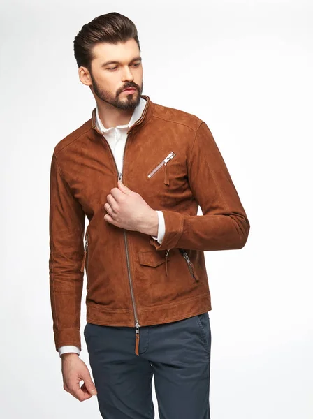 Fashion portrait of handsome male model with dark hair, beard and eyes, wearing white shirt, orange brown jacket, posing on white background