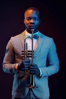 Neon trompet onun elinde çiçek papyon ile ekose ceketli yakışıklı siyah jazzman portresi. Turuncu ve mavi stüdyo ışık 