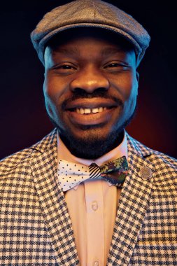 Komik yüz çiçek papyon ve vintage cap ile ekose ceket ve beyaz gömlek gülümseyen yakışıklı siyah jazzman Studio neon portresi 