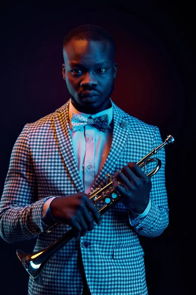 Neon portrait of handsome black jazzman in plaid jacket with floral bow tie and with trumpet in his hands. Orange and blue studio light