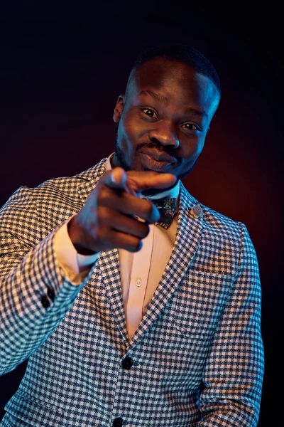 Neon portrait of handsome black man in white shirt and plaid jacket with floral bow tie mocking finger at you.