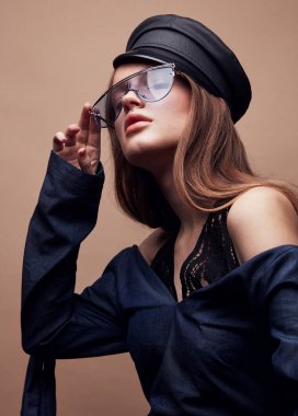 Moda portre siyah deri bere şapka, denim bluz ve mavi retro güneş gözlüğü güzel genç kadın 
