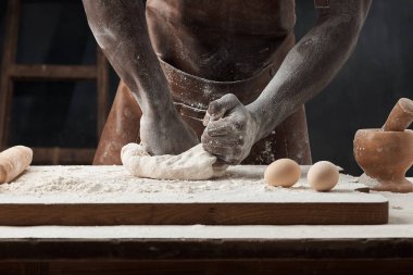 Siyah bir adamın elleri masada hamuru yumurta, un, merdane ve değirmenle yoğuruyor.