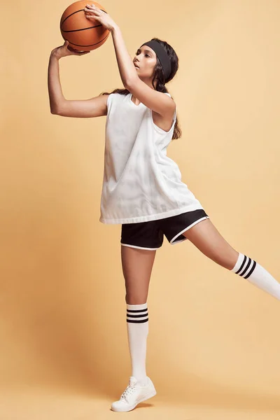 beautiful dark-skinned girl on a yellow background in white sports shirt, black shorts, white high socks and sneakers jumping with a basketball ball