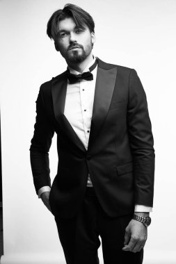 Siyah beyaz, kısa sakallı, siyah saçlı yakışıklı bir adamın portresi. Siyah smokin giyiyor. Siyah papyonlu, beyaz, klasik bir gömlek.