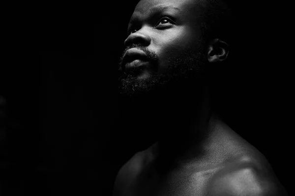 black and white portrait of a handsome black man with naked sports torso looking in the left on dark background