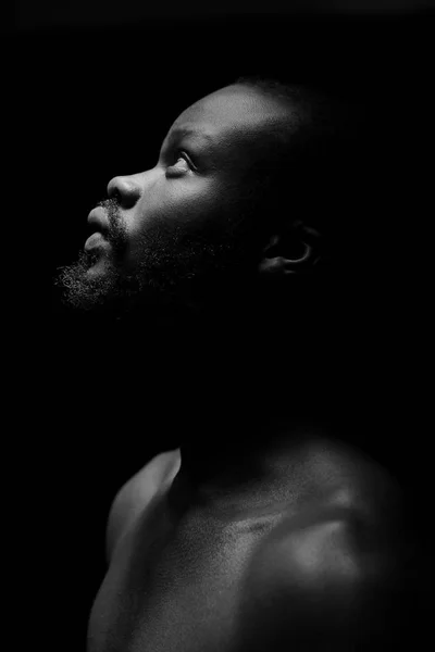 black and white portrait of a handsome black man with naked sports torso looking in the left on dark background