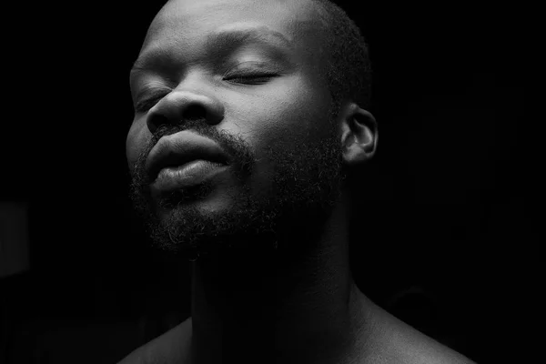 black and white portrait of a handsome black man with closed eyes on dark background