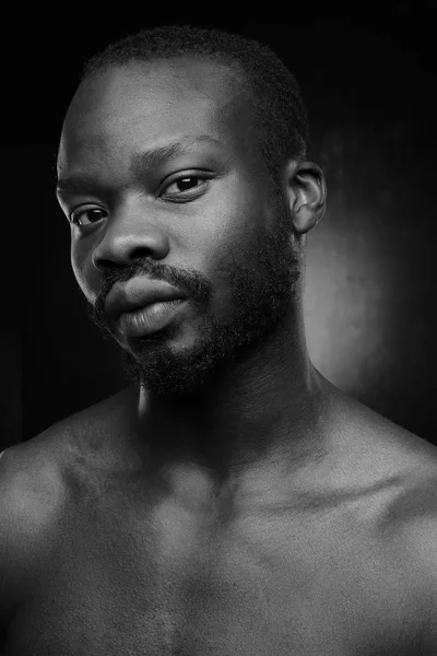 black and white portrait of a handsome black man with naked sports torso looking in the camera on dark background