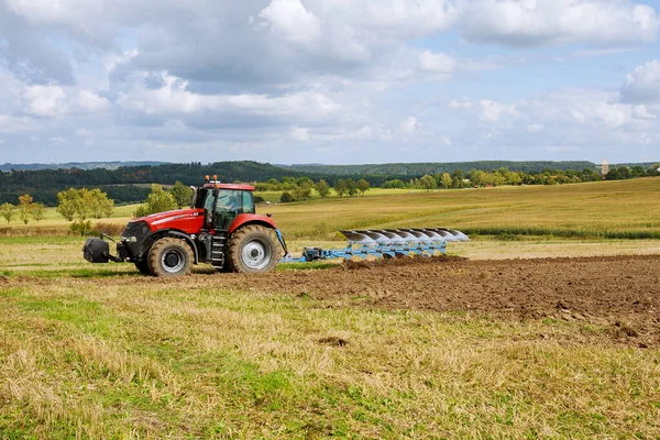 Landwirt mit rotem Traktor bereitet Land mit Pflug für die Aussaat vor — Stockfoto