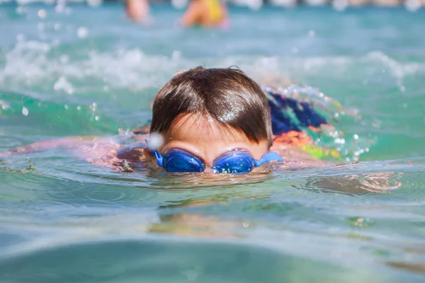 Holidays at sea. A boy in blue swimming goggles swims in the sea.