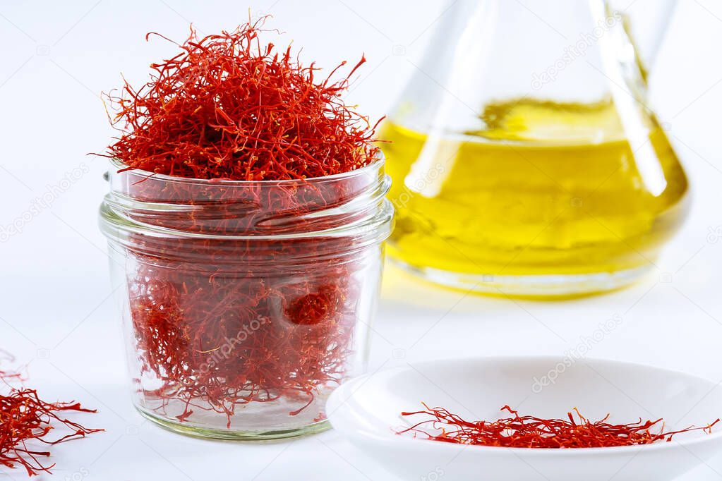 dried saffron threads in a glass bottle and oil extract on a white