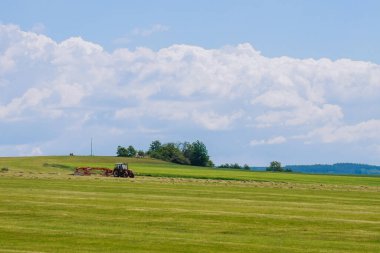 Kırmızı bir traktör kuru otları temizler ve yükleme ve taşıma için saman yerleştirir..