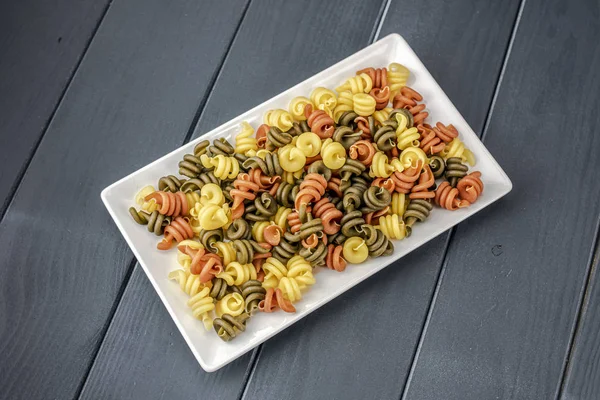 Piatto di pasta cruda colorata e verdure pronte per essere cotte — Foto Stock