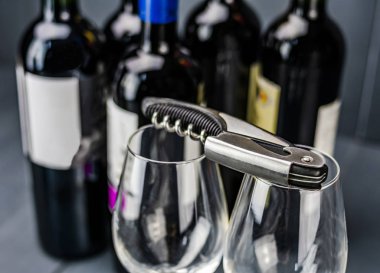 Şarap kadehlerinde tirbuşon ve arka planda kırmızı şarap şişeleri.