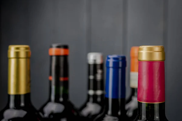 Red wine bottlenecks labeled of different colors on gray wooden