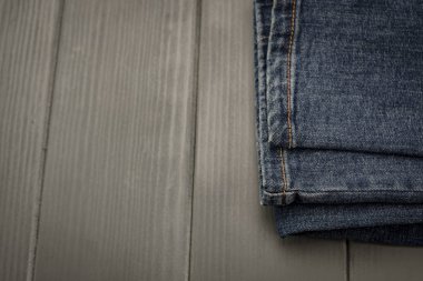 Gri ahşap arka planda katlanmış kot pantolonlar.