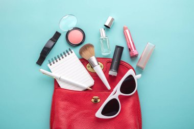 Open woman fashion bag with stuffs on blue background