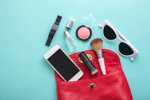 Red woman bag with cosmetic and stuffs on blue background — Stock Photo, Image