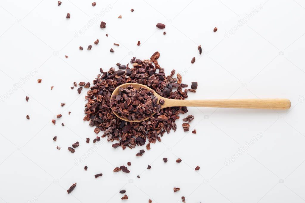 Cacao nibs on wood spoon on white background, top view