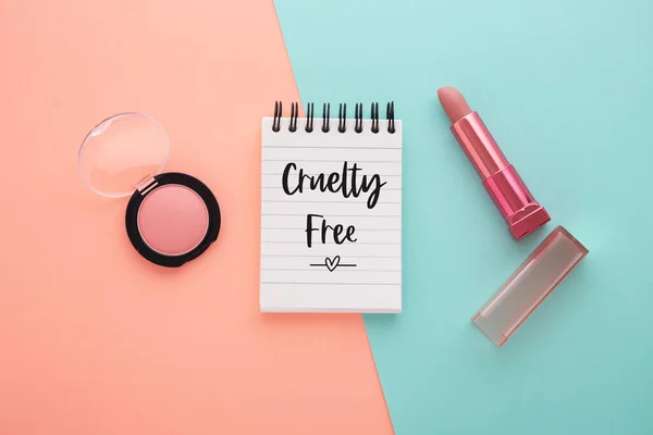 Cruelty free word with lipstick and blush on coral and blue background, flat lay