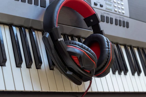 Fones de ouvido preto e vermelho estão nas chaves do sintetizador. Fones de ouvido elegantes no fundo das teclas de piano. Teclado piano com auscultadores para música . — Fotografia de Stock