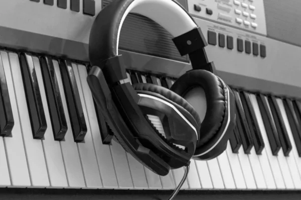 Fekete-fehér fotó. A fejhallgató a szintetizátor kulcsán van. Stílusos fejhallgató a zongora kulcsok hátterén. Zongora billentyűzet fülhallgatóval a zenéhez. Home zenei stúdió. — Stock Fotó