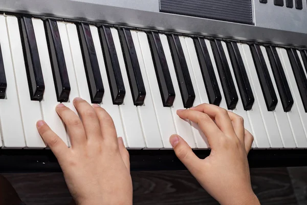 Közelről, ahogy a baba kezei zongoráznak. Egy gyerek kezei, amint szintetizátor billentyűzetén játszik. Közelkép egy baba kezéről és fekete-fehér zongorakulcsokról.. — Stock Fotó