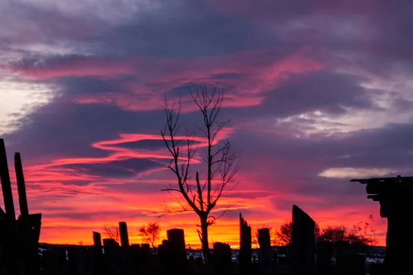 Tramonto rosso-blu con nuvole scure alla periferia del villaggio. I contorni di una vecchia recinzione rotta sullo sfondo di un'alba di fuoco. Artisticamente sfocato — Foto Stock