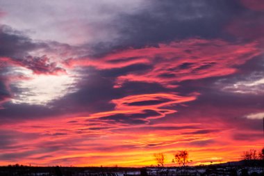 Köyün eteklerinde koyu bulutlu kırmızı-mavi gün batımı. Karanlık kış kırsal silueti ve güzel bir gündoğumu. Sanatsal olarak bulanık
