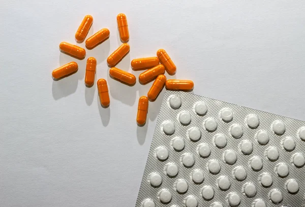 Verstreute orangefarbene Kapseln und Blisterverpackungen weißer Tabletten auf weißem Papier. Layout für Sonderangebote, Werbung, Webhintergrund. das Konzept der Medizin, der Apotheke, des Gesundheitswesens. Leerraum für Text — Stockfoto